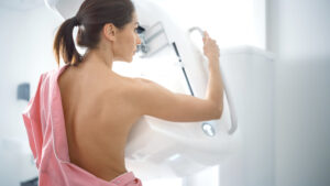 A patient undergoing a mammogram while positioned at a breast imaging machine for breast screening.