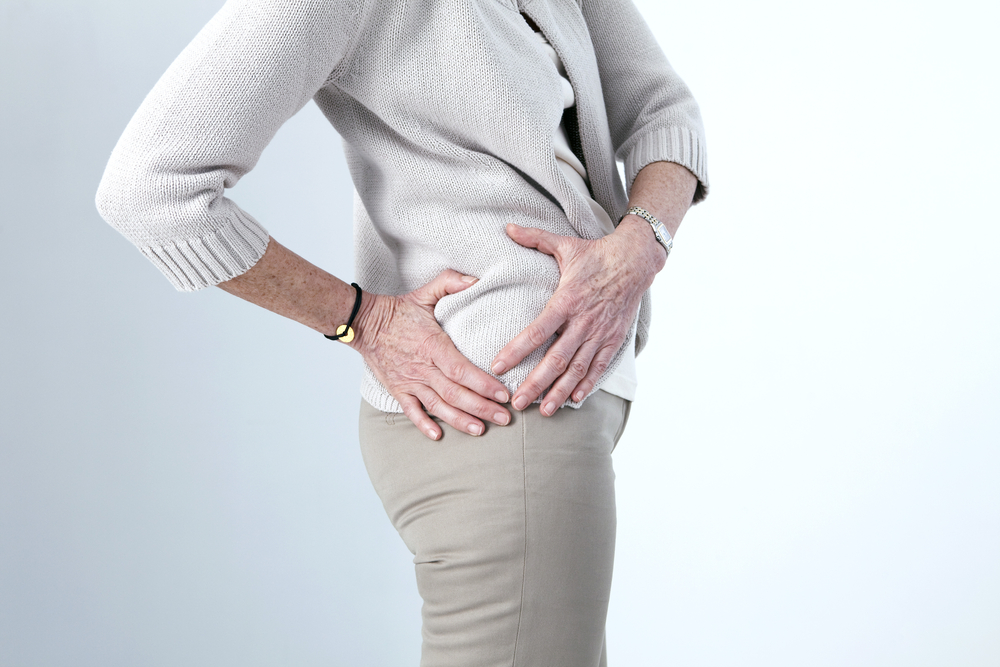 A person holding the lower back and hip area, illustrating back pain or a musculoskeletal condition affecting the lower spine or pelvis.