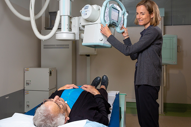 Technologist adjusting an X-ray machine above an elderly patient lying on an examination table.