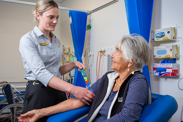 A nurse applying a tourniquet to an elderly patient’s arm while preparing for a medical imaging procedure.