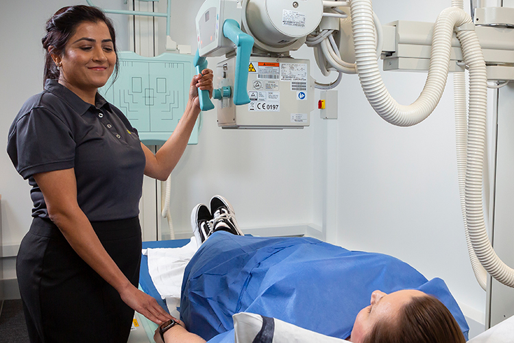 Technologist positioning an X-ray machine above a patient lying on an imaging table.