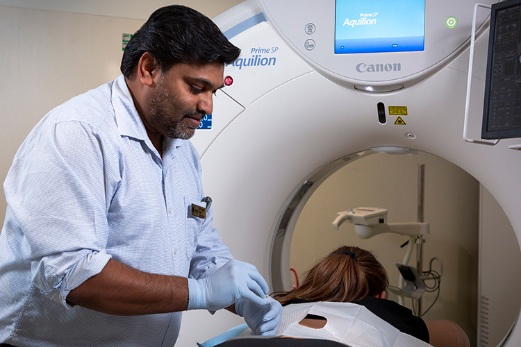Radiologist performs an interventional procedure on a patient laying down on a CT machine bed.