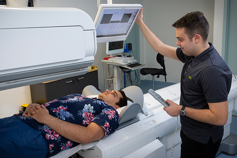 A radiographer positions equipment above a patient lying on a diagnostic imaging table.