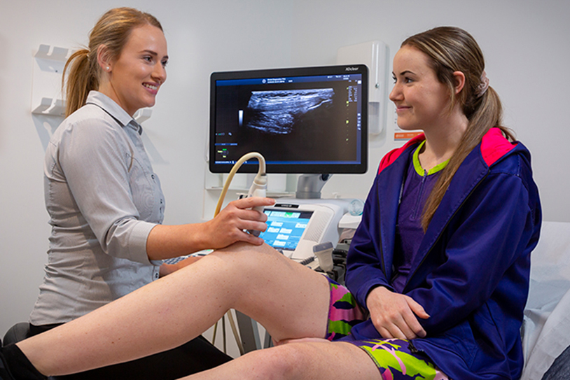 A sonographer performs an ultrasound scan on a patient’s knee in a clinical examination room.