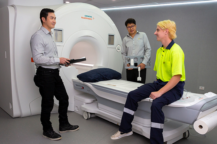 Two medical health professionals prepare a patient seated on an MRI table for an upcoming scan.