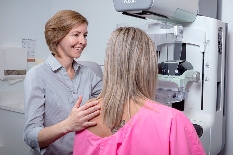 A radiographer guides a patient through a mammogram procedure.