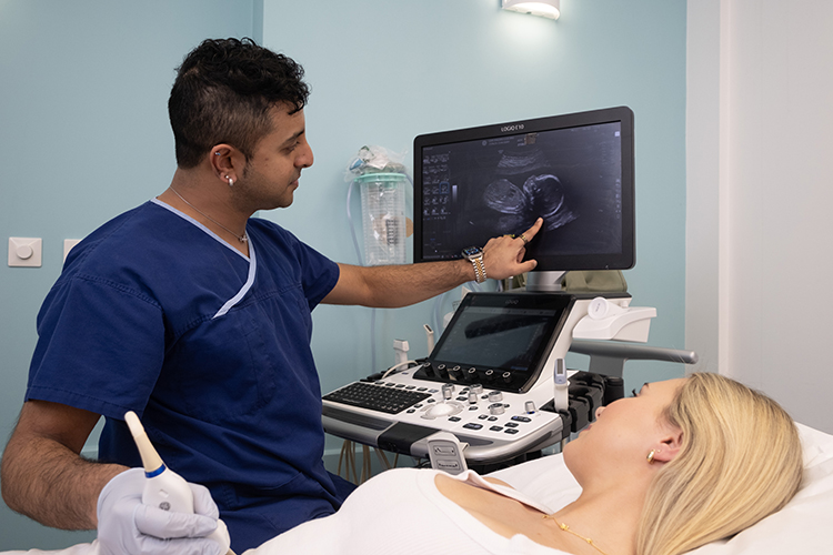 An ultrasound examination in progress, with a sonographer explaining the images displayed on the monitor while the patient lies on the examination bed.