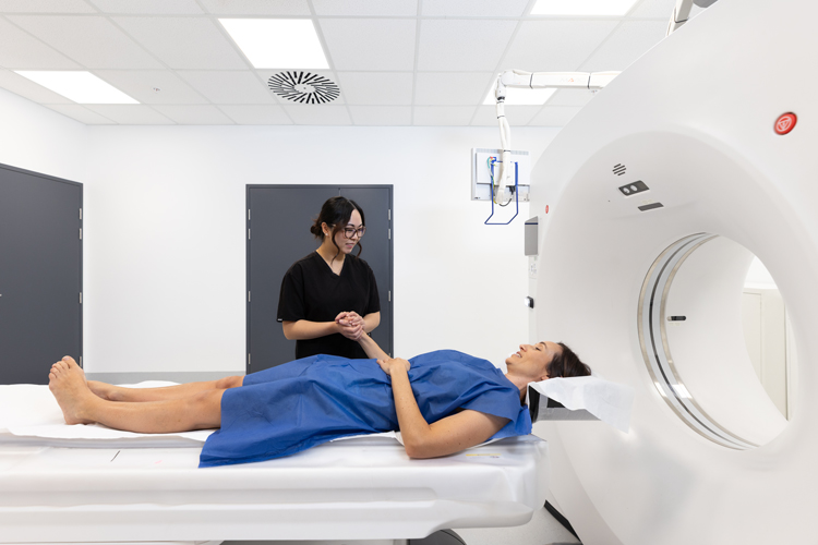 CT Radiographer supporting patient laying down by holding her hand. Patient is about to get her CT scan.