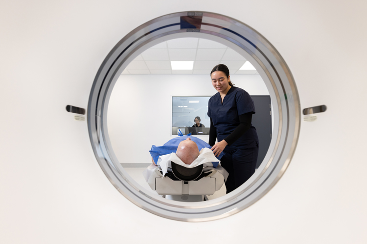 View through a CT scanner showing a patient on the scanning table as a healthcare professional assists with positioning before the scan.